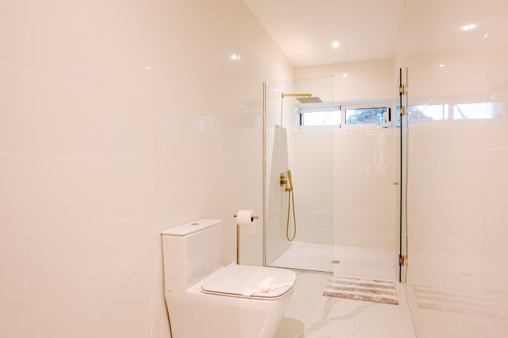 Modern bathroom with toilet, glass shower, and white tiled walls and floor.