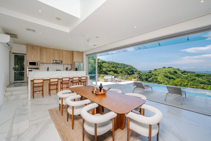 Modern open kitchen and dining area with pool and scenic mountain view through large windows.