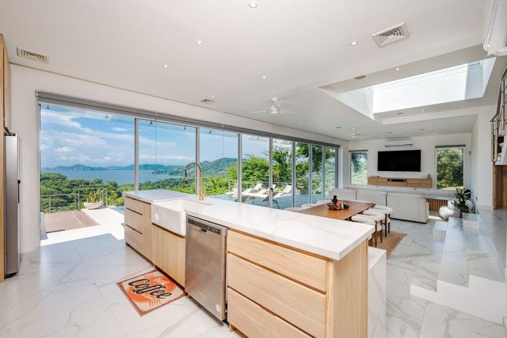 Modern kitchen with island, open living area, floor-to-ceiling windows, and a scenic ocean view.