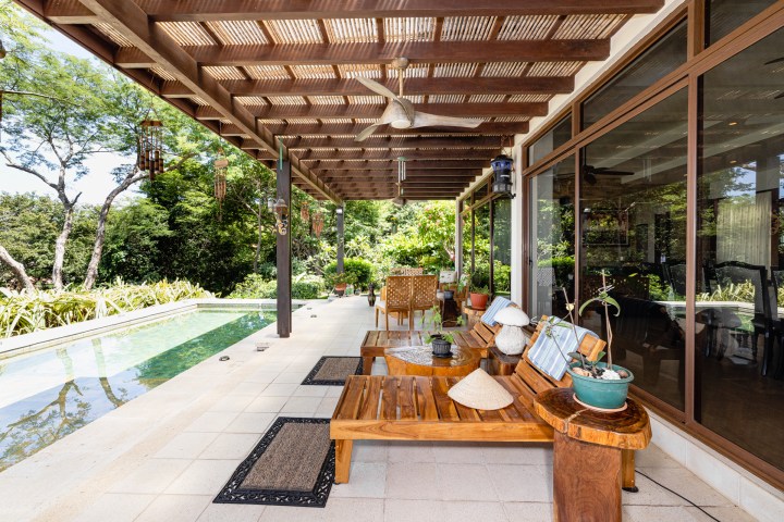 Patio with wooden furniture, pergola, pool, and lush garden view.