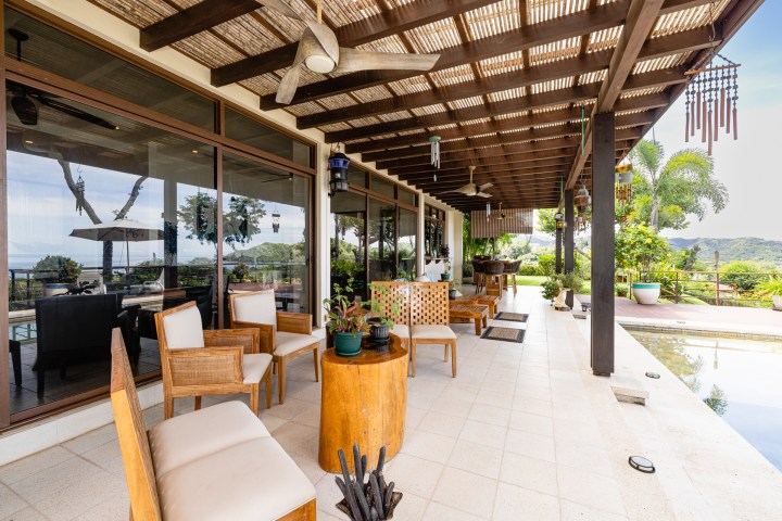 Outdoor patio with wooden furniture and pergola, overlooking a pool and scenic landscape.