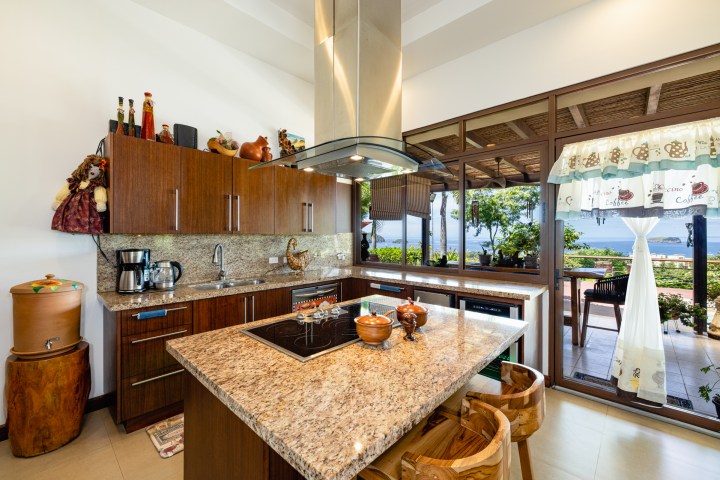 Modern kitchen with wood cabinets, granite countertops, and ocean view through large windows.