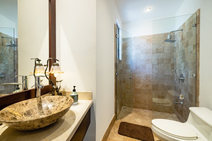 Bathroom with stone sink, mirror, glass shower, and toilet.