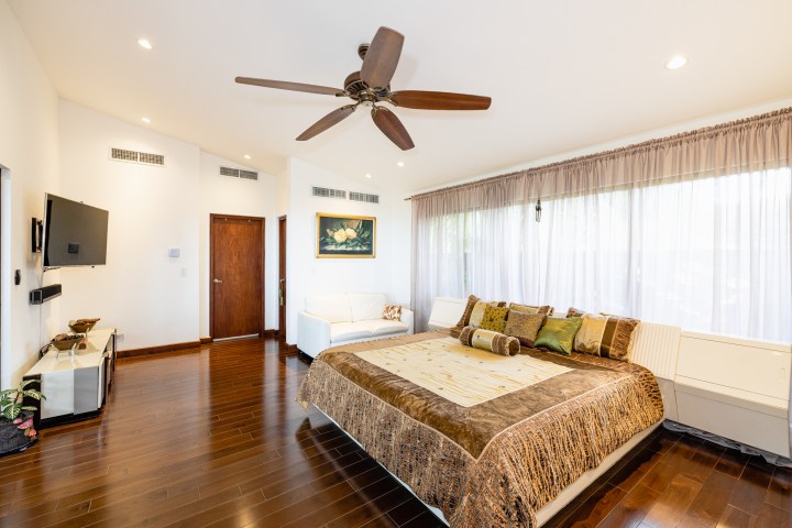 Modern bedroom with ceiling fan, large bed, flat screen TV, and white curtains.