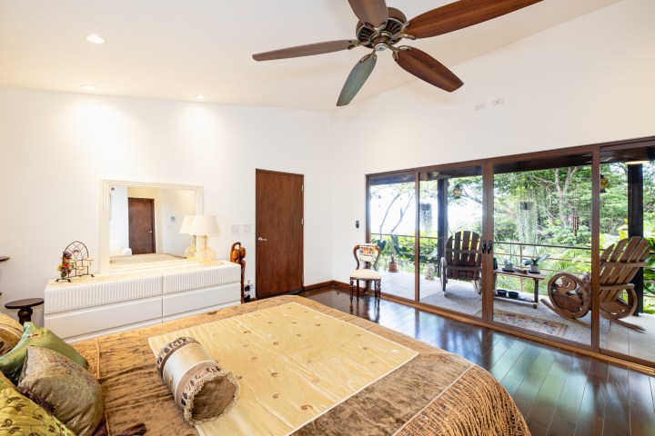 Bedroom with a large bed, ceiling fan, dresser, and glass doors opening to a patio with chairs.