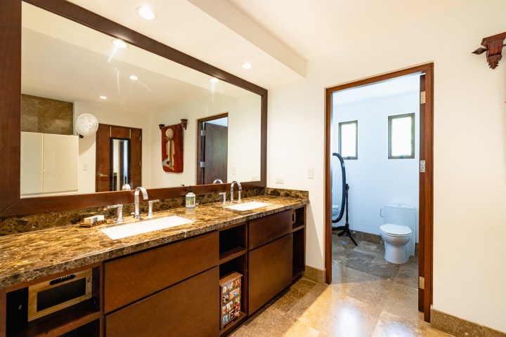 Bathroom with double sinks, large mirror, and adjoining toilet area.