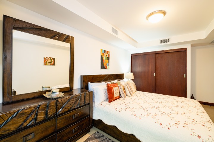 Modern bedroom with wooden dresser, large mirror, floral bedspread, and abstract wall art.
