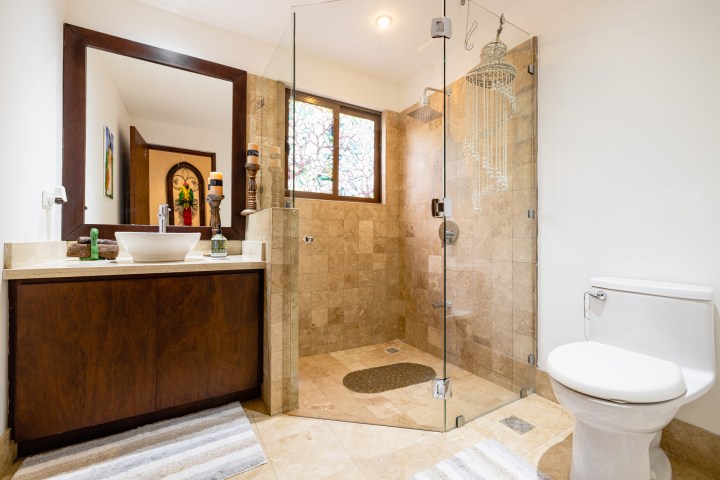 Modern bathroom with glass shower, toilet, and sink on wooden vanity, lit by ceiling light.