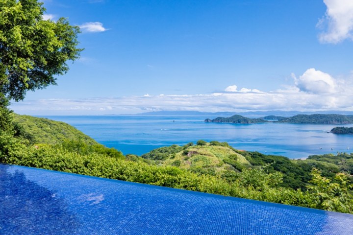 Infinity pool overlooking a scenic ocean view with lush green islands and blue sky.