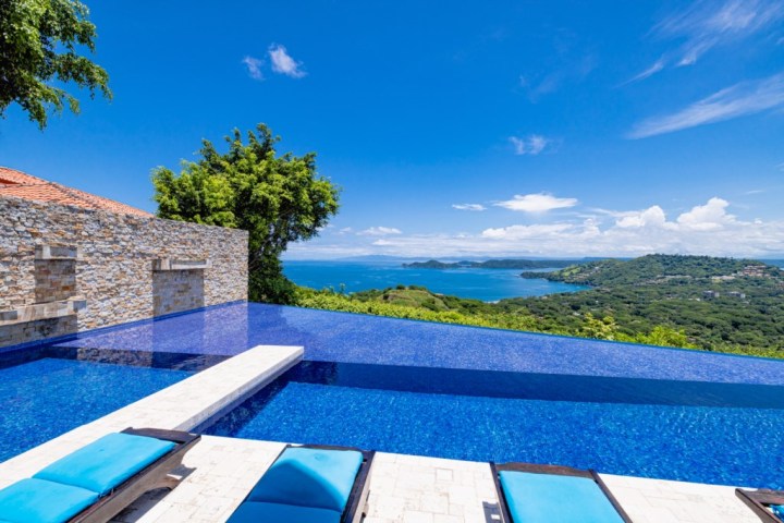 Infinity pool with sea view and lounge chairs under a clear blue sky.