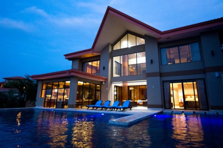Modern house with large windows and a lit swimming pool at dusk.