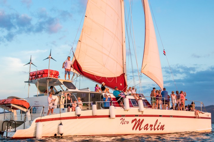 Catamaran with passengers sailing under sunset sky.