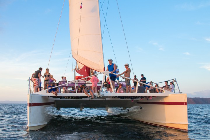 A group of people on a catamaran sailing on the ocean under a clear blue sky.