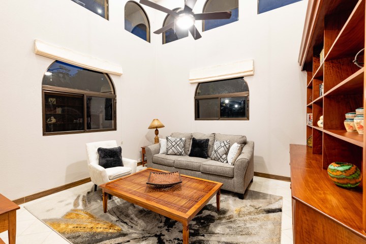 Cozy living room with gray sofa, armchair, wooden coffee table, and shelves under a ceiling fan.