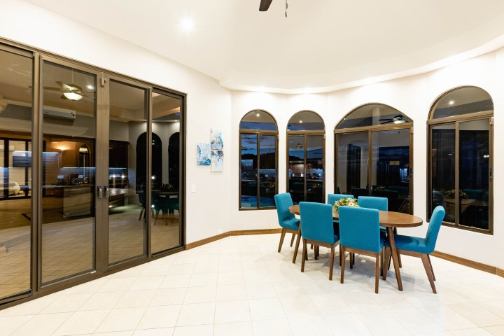 Dining area with blue chairs and large windows overlooking a night view.