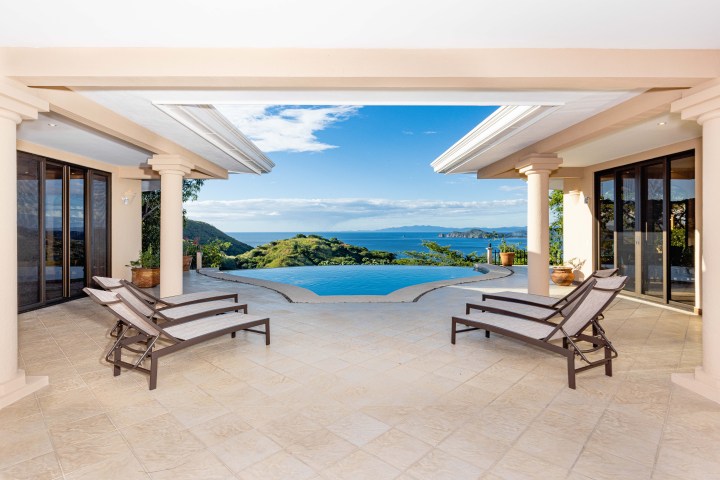Patio with chairs overlooking an infinity pool and ocean view under a clear blue sky.