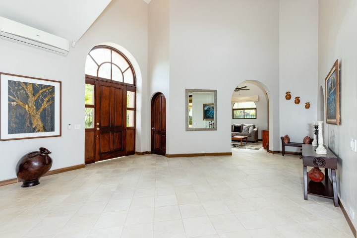 Spacious foyer with arched wooden door, art, and beige tiles, leading to a living room.