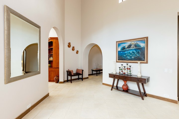 Spacious hallway with arches, a mirror, painting, console table, and seating.
