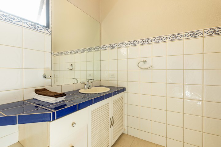 Bathroom with blue-tiled countertop, white sink, mirror, and patterned tile backsplash.