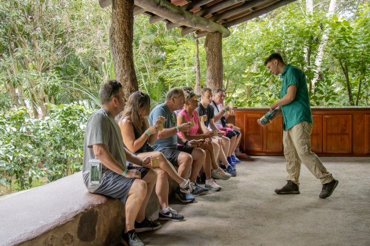 Group of people sitting outside, tasting drinks with a guide on a porch.