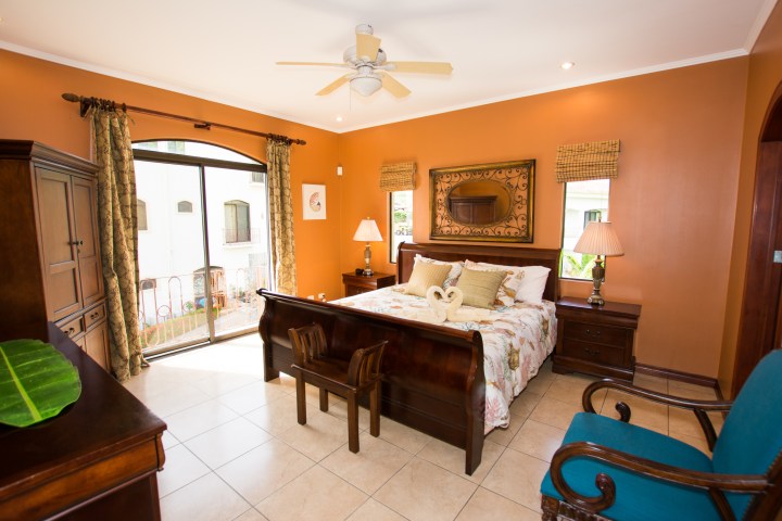 Cozy bedroom with orange walls, wooden bed, and a large window with curtains.