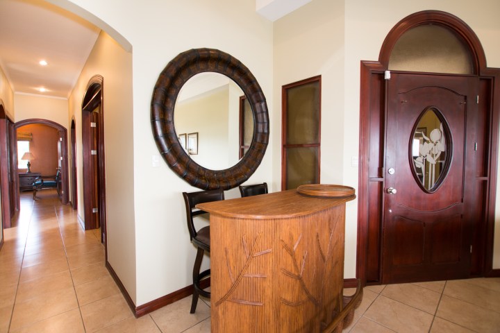 Interior with wooden bar, decorative mirror, and hallway; tiled floor, arched doors visible.