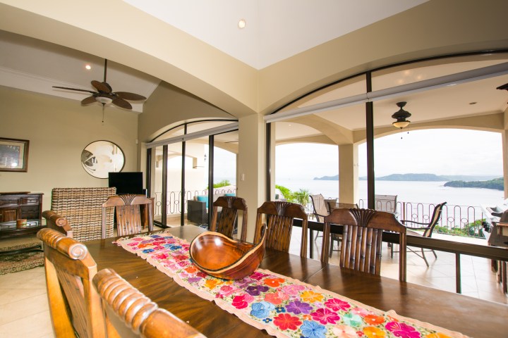 Dining room with wooden table, colorful runner, ocean view through large windows.