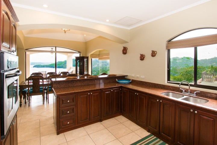 Spacious kitchen with dark wood cabinets, granite countertops, and a view of a dining area and outdoor scenery.