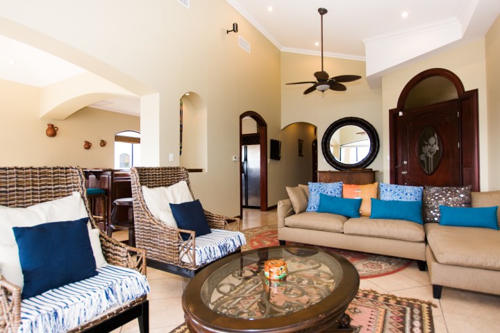 Spacious living room with wicker chairs, sofa, ceiling fan, and decorative cushions in warm tones.