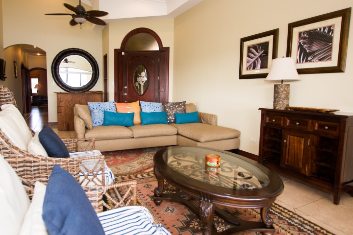 Cozy living room with a beige sofa, colorful cushions, wicker chairs, glass coffee table, and wall decor.