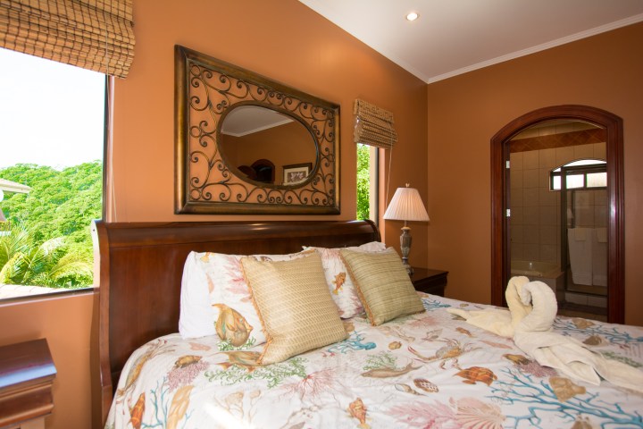 Cozy bedroom with orange walls, decorative mirror, and bed with floral bedding and swan towel art.