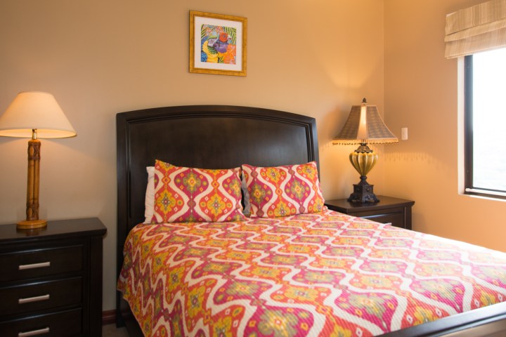 Bedroom with colorful bedspread, two lamps, and framed artwork on wall.