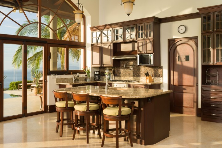 Bright kitchen with wooden cabinets, large island, and ocean view through arched windows.