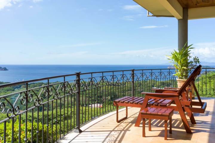 Terrace with two wooden loungers overlooking ocean and greenery.