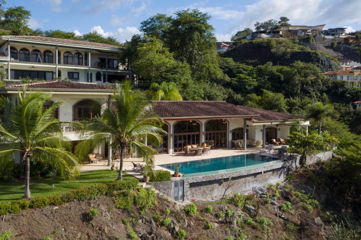Luxurious hillside villa with pool, palm trees, and lush greenery.