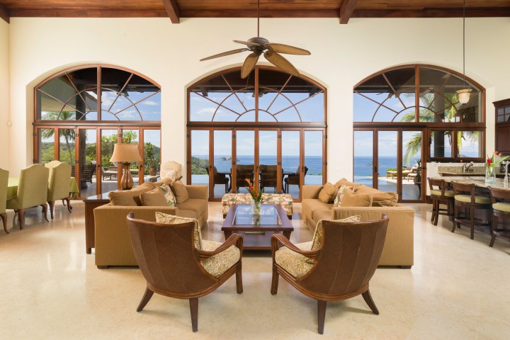Spacious living room with ocean view, large windows, sofas, and a ceiling fan.