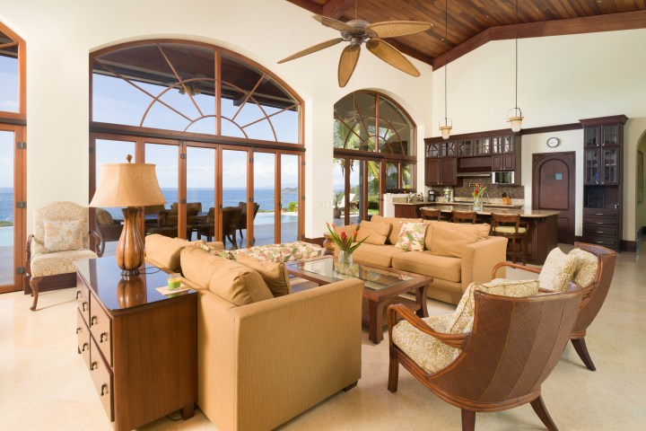 Open-plan living room with sofas, dining area, and ocean view through large arched windows.