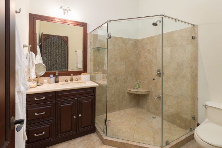 Modern bathroom with glass shower, dark wood vanity, and beige tiles.