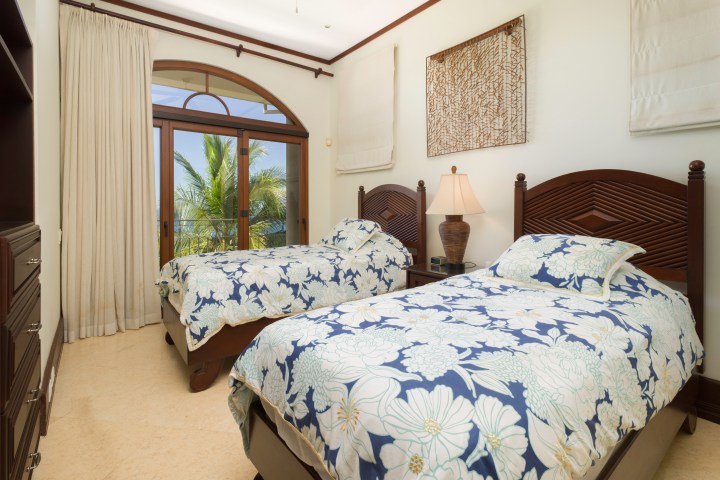 Bedroom with two twin beds, floral covers, and a window with a palm tree view.