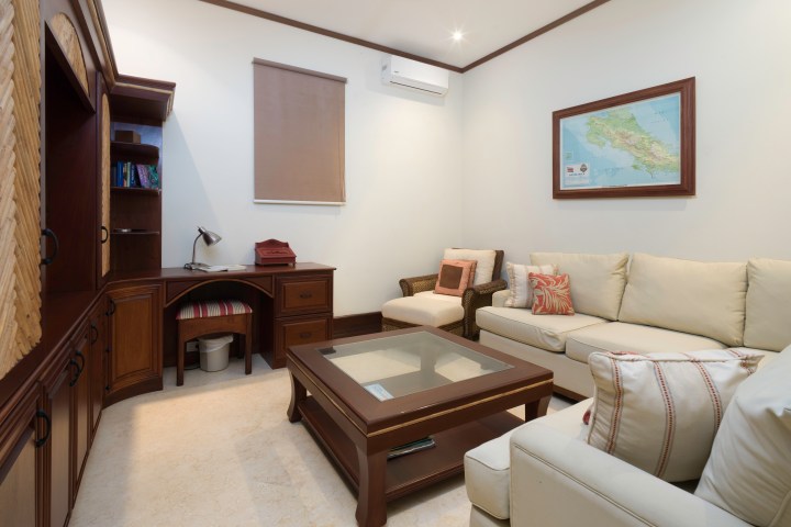 Small cozy living room with a couch, desk, and wall map, featuring a glass coffee table and bookshelf.