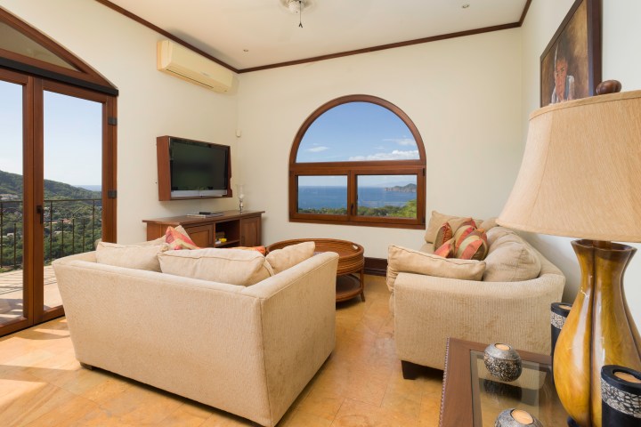Bright living room with beige sofas, sea view window, and wall-mounted TV.