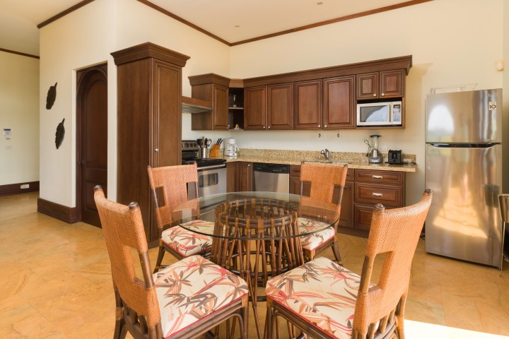 Kitchen with wooden cabinets, round glass table, wicker chairs, and stainless steel appliances.