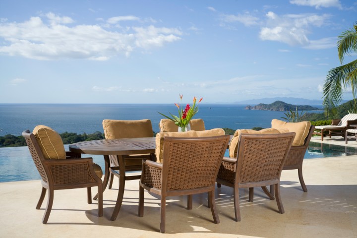 Outdoor dining table with wicker chairs overlooking the ocean and mountains.