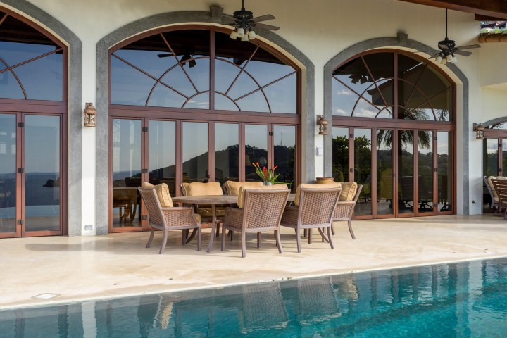 Patio with wicker furniture, arched windows, and pool overlooking a scenic view.