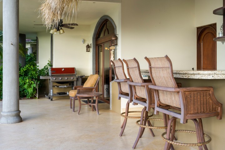 Outdoor patio with wicker chairs, a bar counter, and a grill in the background.