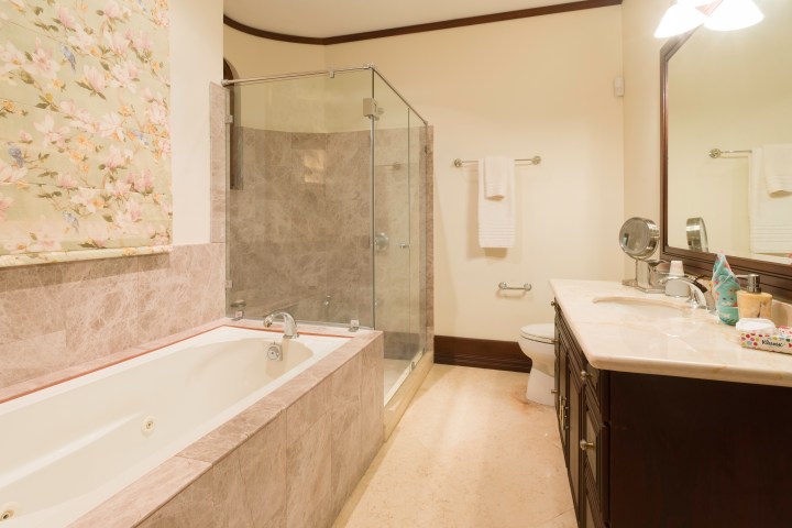 Bathroom with tub, glass shower, vanity, toilet, and floral blind.