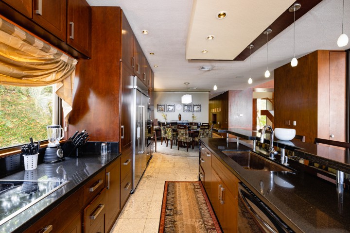 Modern kitchen with wooden cabinets, black countertops, and stainless steel appliances, leading to a dining area.