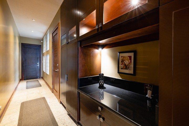 Hallway with dark cabinets, framed art, and a mat on light tiled floor.