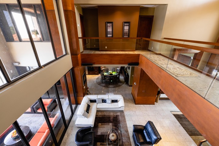 Modern living room with white and black furniture, wooden accents, large windows, and upper-level balcony view.