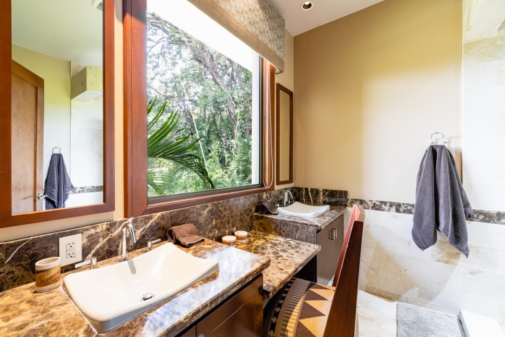 Modern bathroom with two sinks, marble countertops, a large window, and towel rack on beige walls.
